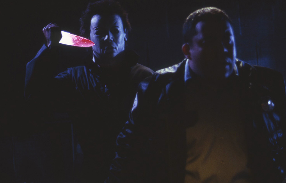 Michael Myers raises a knife behind Freddie inside the house.