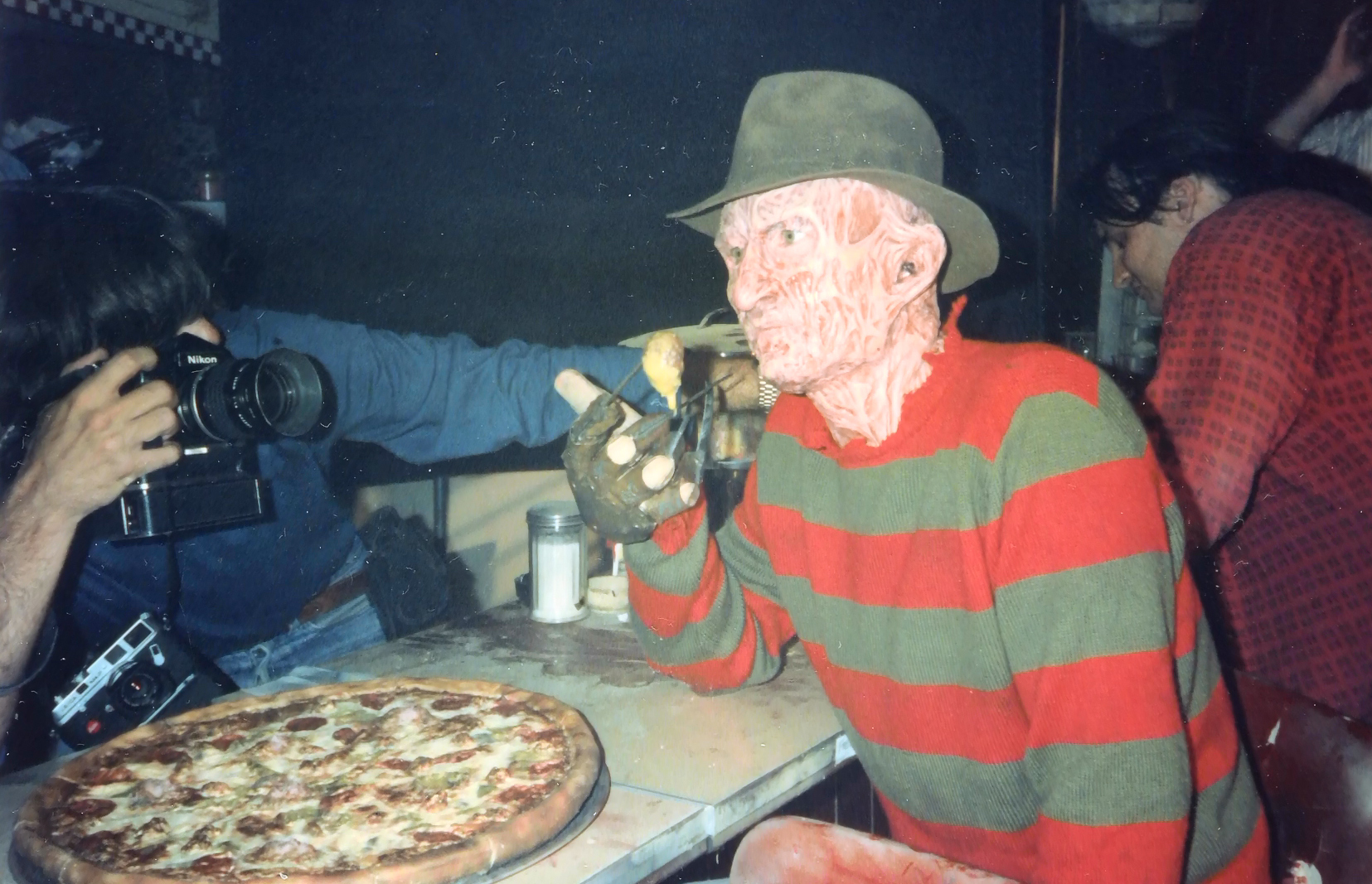 Robert Englund at the diner table with pizza while a photographer works alongside him.
