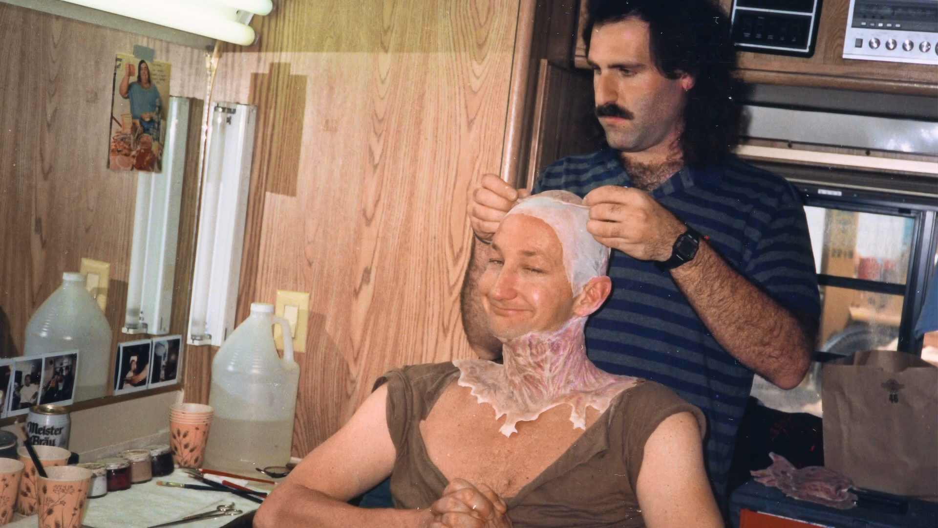 An artist fits the forehead appliance while Robert Englund sits in the makeup chair.
