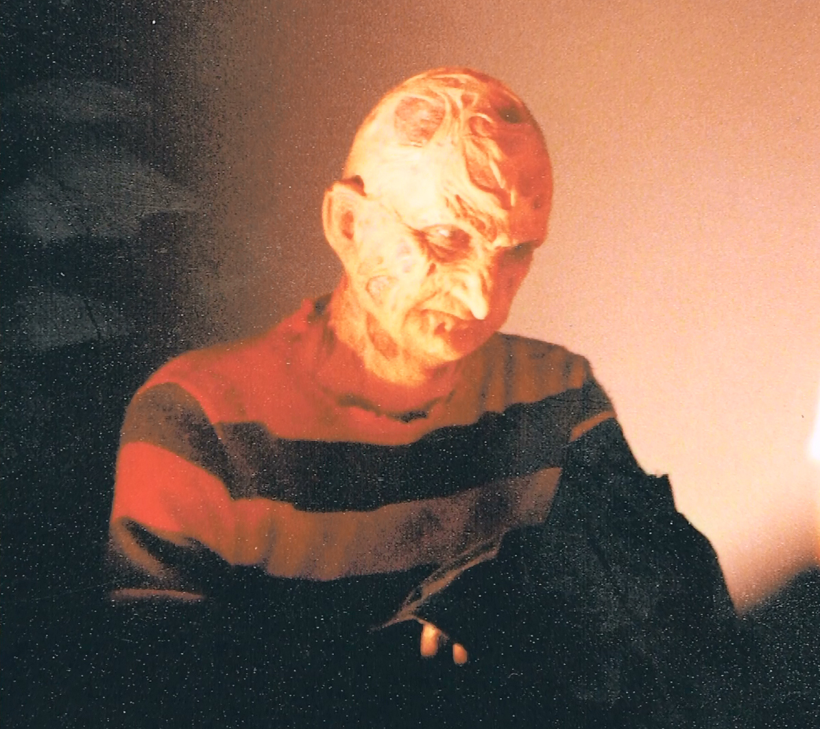 Robert Englund seated in Freddy makeup between setups under warm lighting.