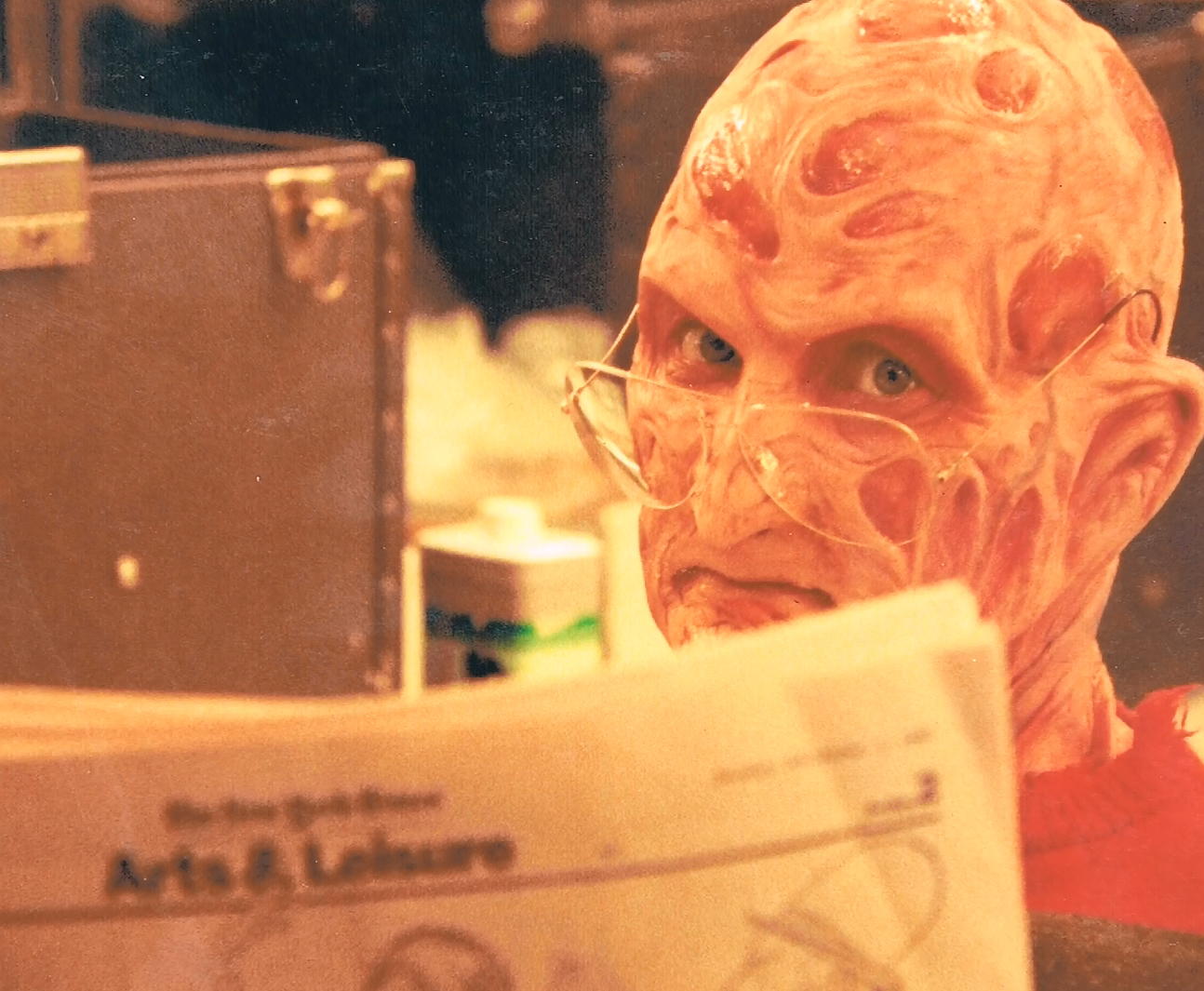 Robert Englund reading a newspaper while seated in the makeup area.