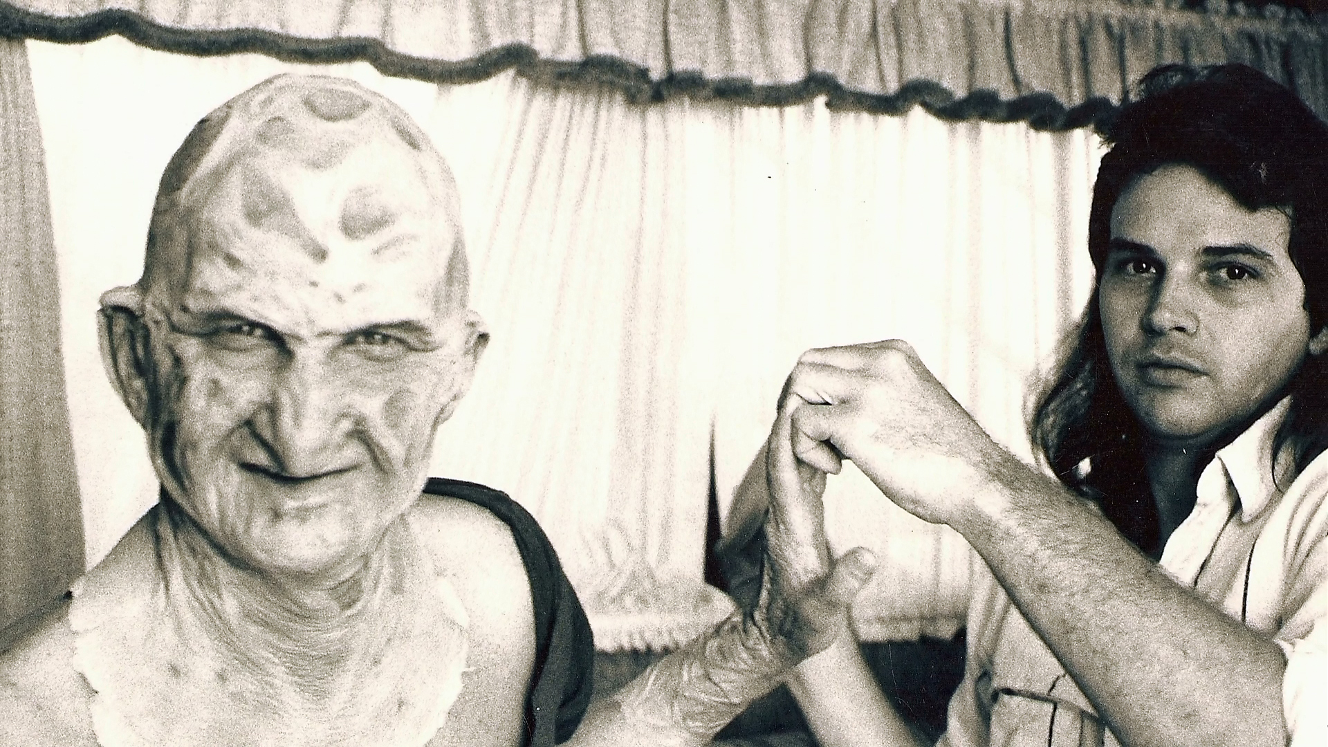 An artist adjusts Robert Englund's sleeve or glove during preparation.