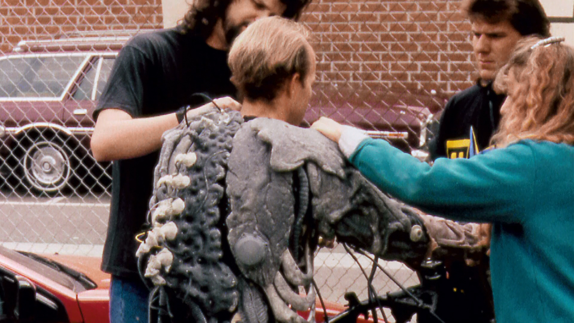 The crew fits the biomechanical costume outdoors, revealing its back construction.