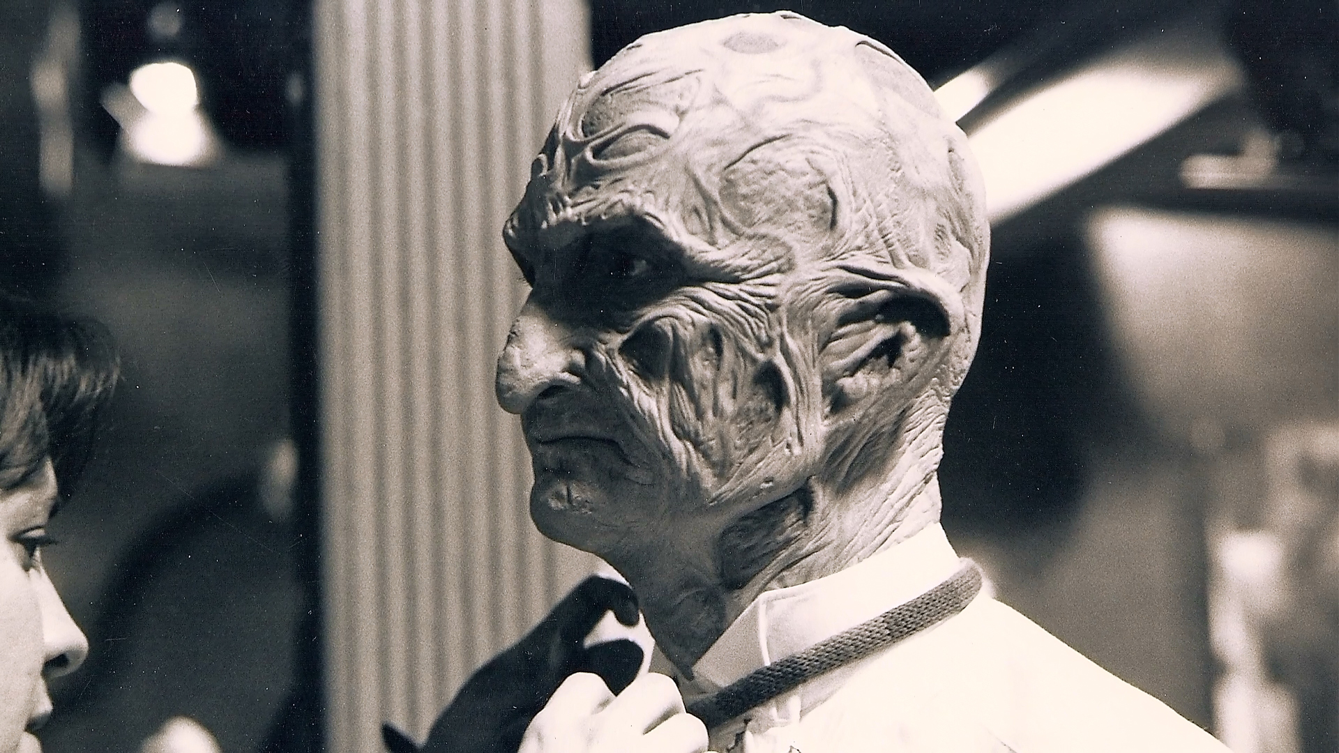 Robert Englund in the chef makeup while an artist works on the collar area.