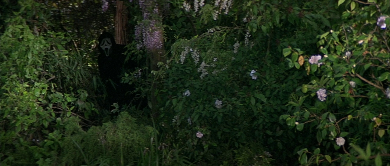 Ghostface partly concealed by foliage. Film frame.