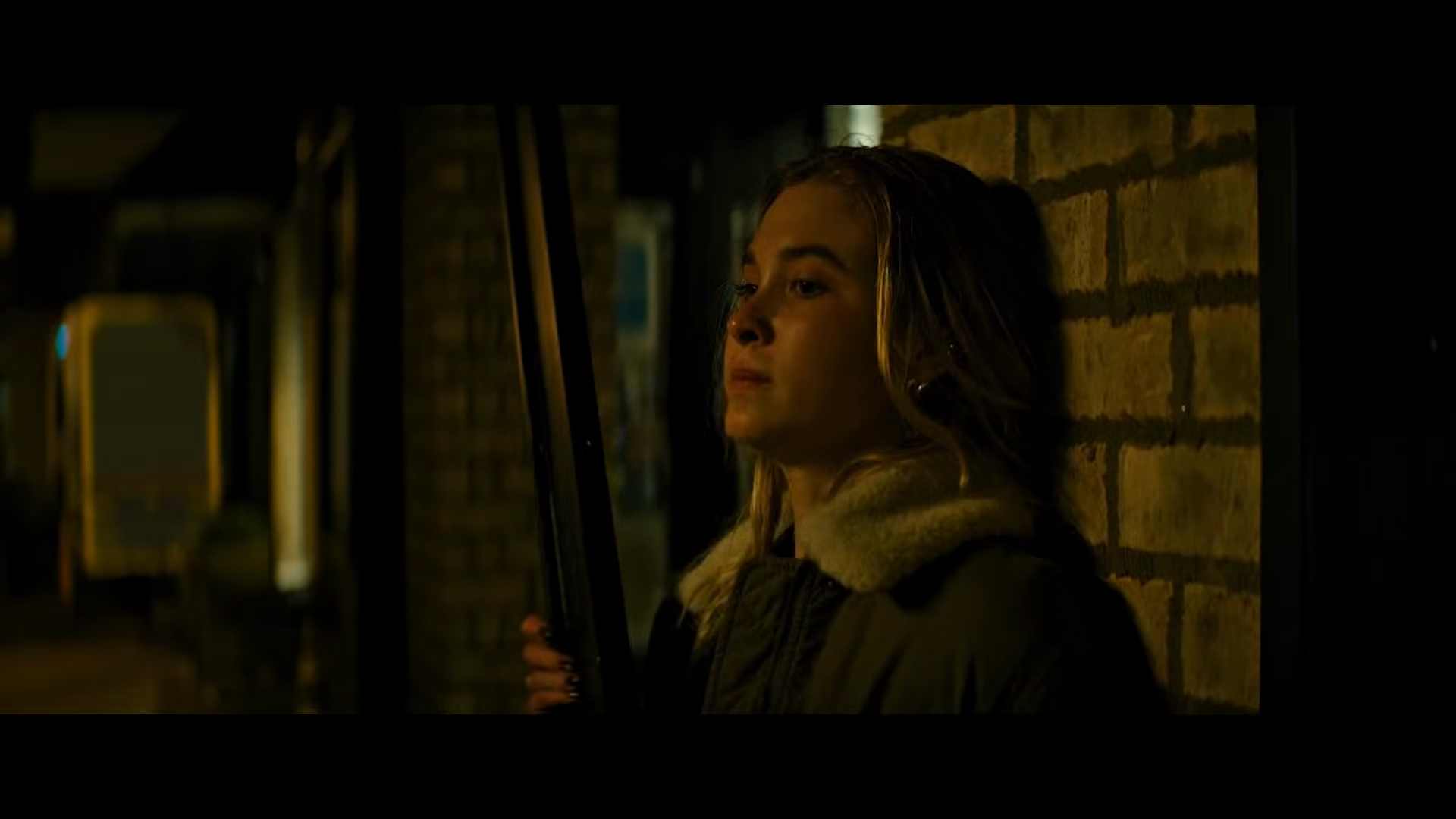 Sidney’s daughter waits beside a brick wall with a shotgun.